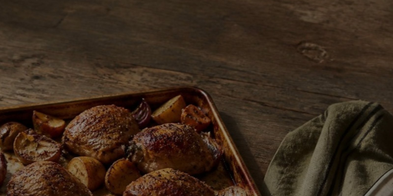 Sheet pan of roasted chicken thighs and potatoes on a wooden table
