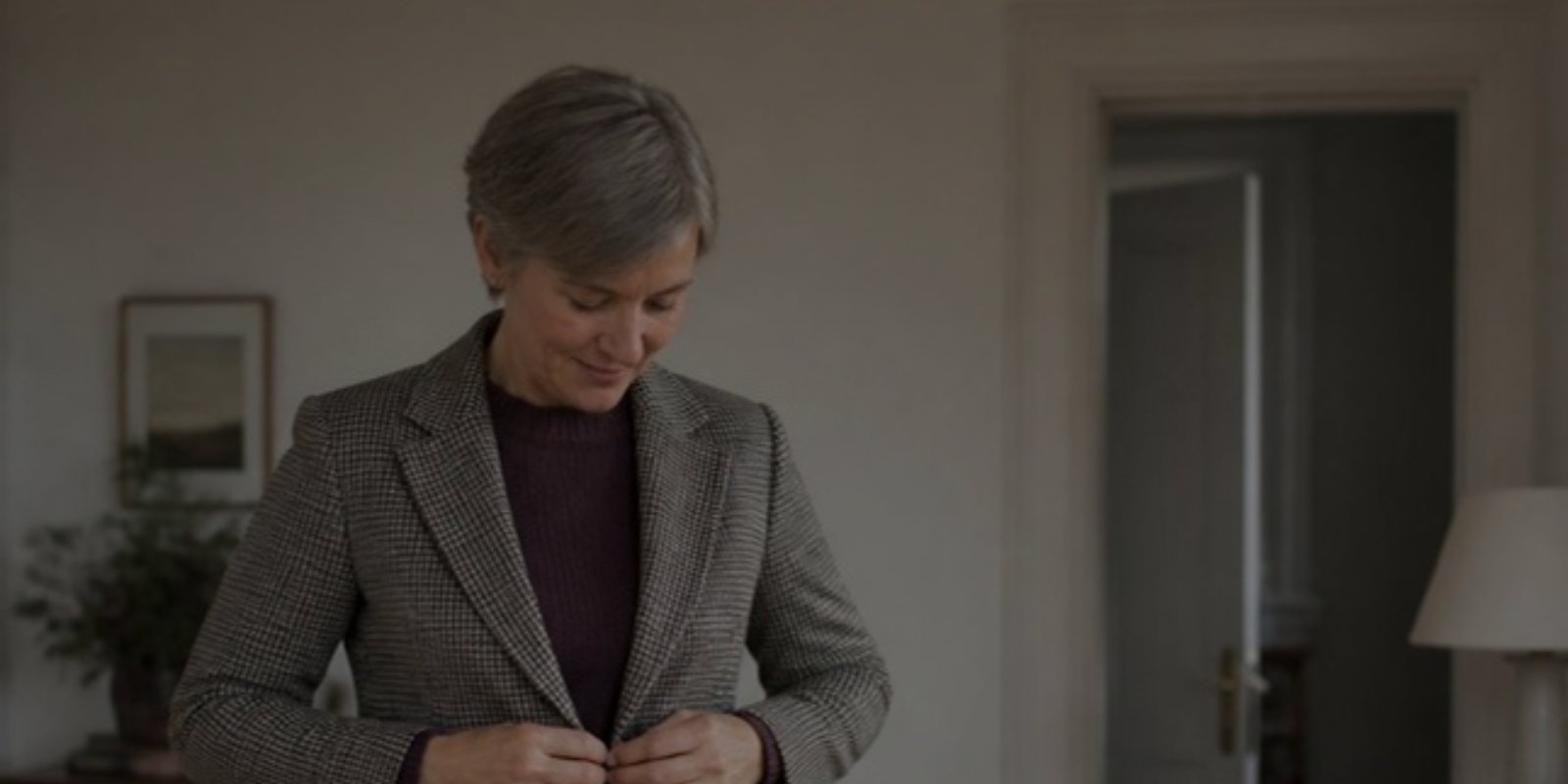 Woman with short grey hair buttoning a check blazer over a plum sweater